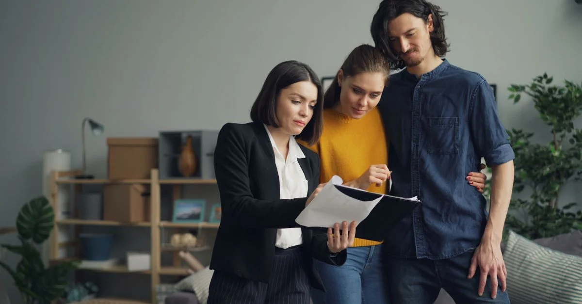 Jeune couple consultant un agent immobilier sur un bien à l'intérieur.