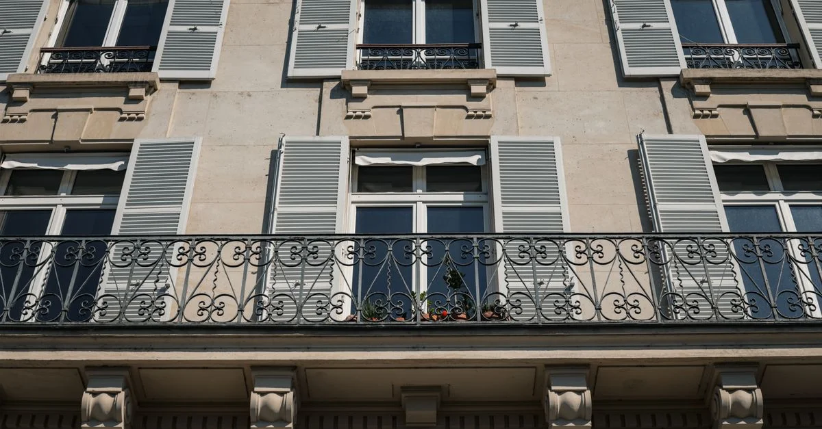 Élégante façade d'appartement parisien avec balcon en fer ornemental et volets dans la ville de Paris.