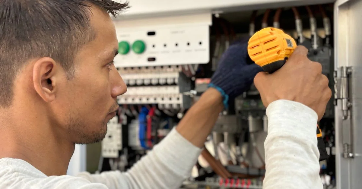 Un technicien concentré utilisant une perceuse sur un panneau électrique, mettant en valeur un savoir-faire expert.