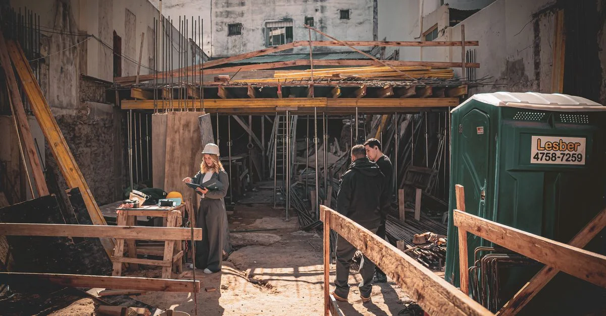 Chantier avec ouvriers et architecte examinant des plans en plein jour.