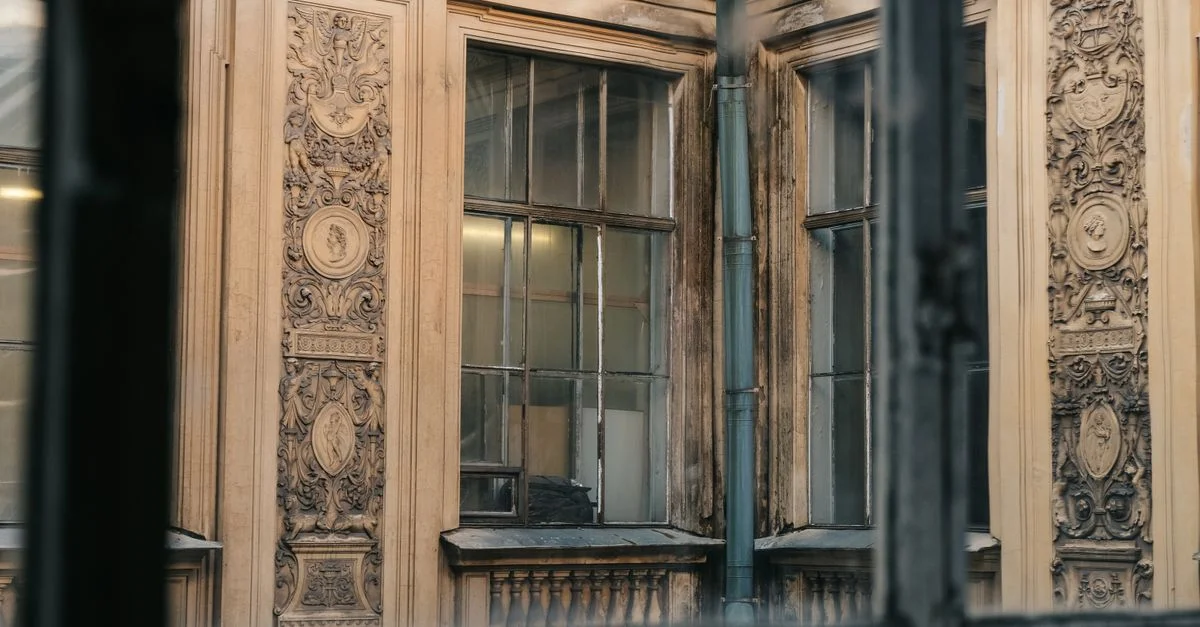 Gros plan sur une façade vintage avec des sculptures détaillées ornées et des cadres de fenêtres vieillissants.