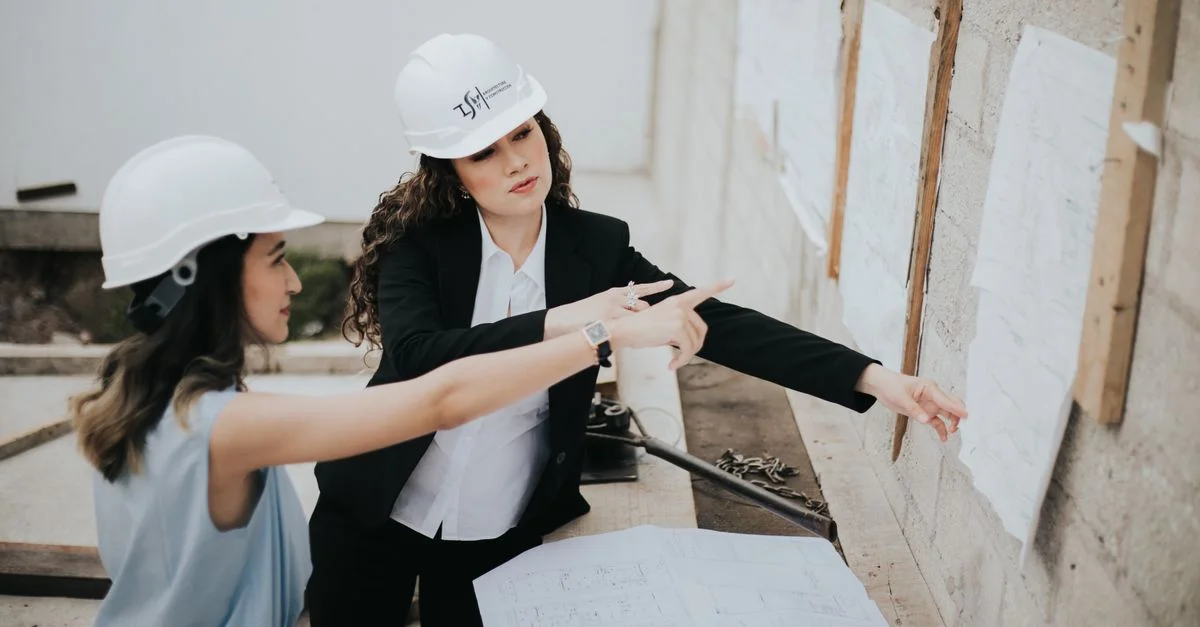 Deux architectes femmes discutant de plans de construction en extérieur, mettant en avant le travail d'équipe et le leadership féminin.