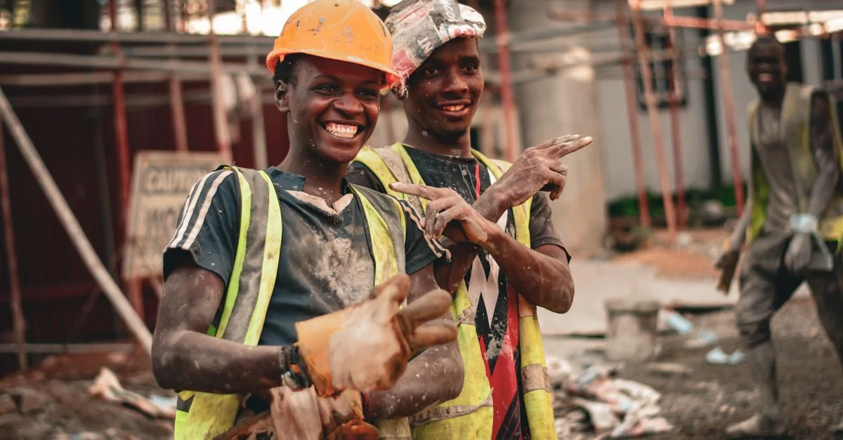 Deux ouvriers du bâtiment souriants en casques et gilets de sécurité pointant avec joie sur un chantier.